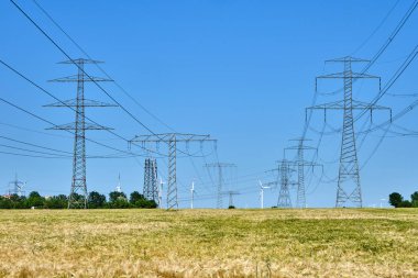 Almanya 'da arkasında rüzgar türbinleri olan elektrik direkleri ve elektrik hatları