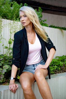 İnce, atletik, uzun, sarışın kız ceketi bankta.