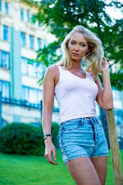 Güzel, zayıf, uzun boylu, şortlu sarışın bir kız yaz parkında dinleniyor.