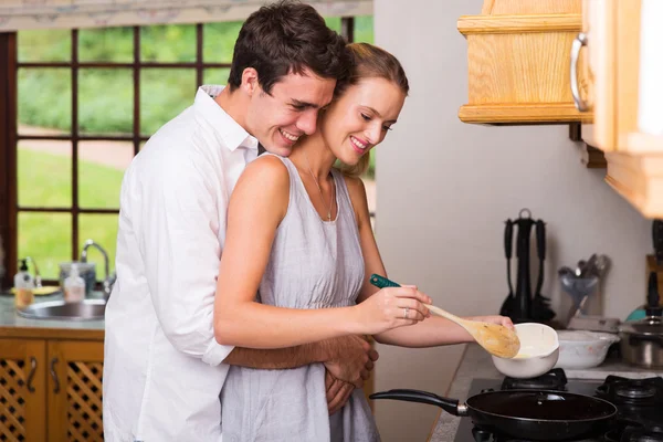 Homme étreignant petite amie pendant qu'elle cuisine pour le petit déjeuner — Photo