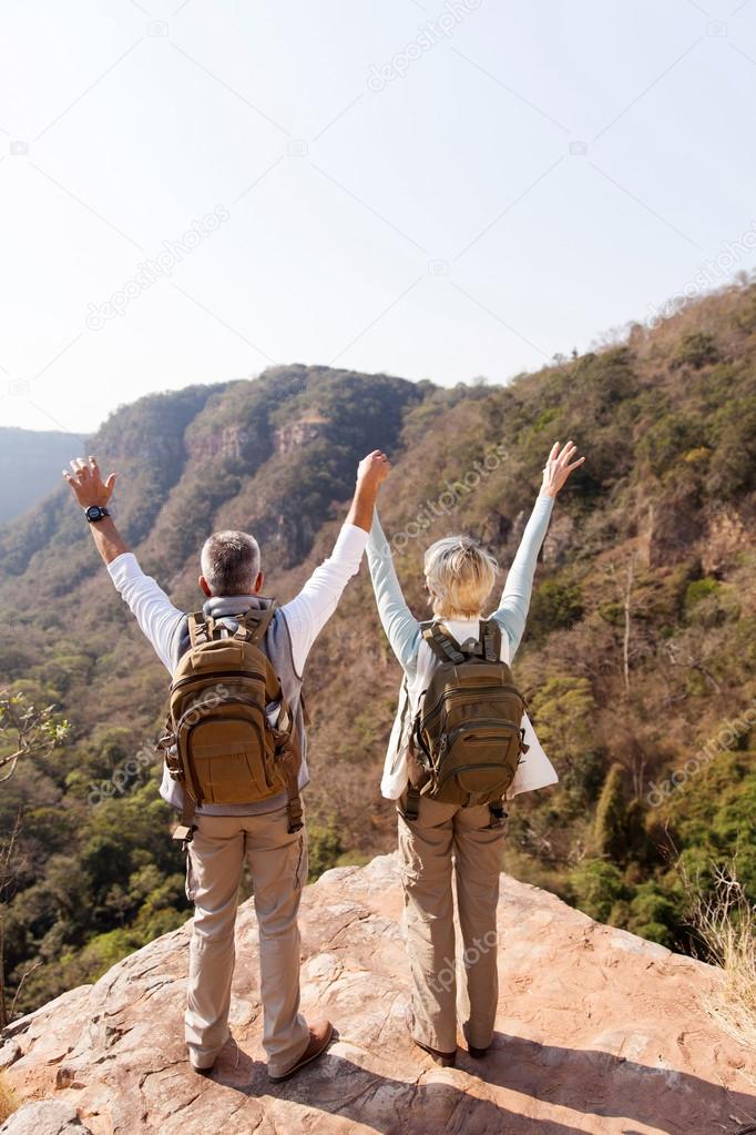 hikers with arms open on mountain cliff