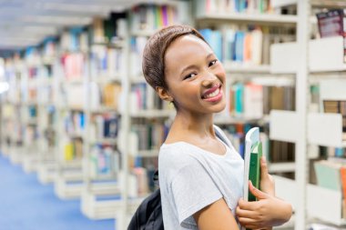 Kitaplığındaki kitap tutan üniversite öğrencisi