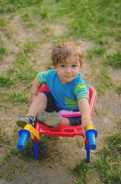 Niño pequeño jugando con carretilla de construcción de plástico para niños de colores — Foto de Stock