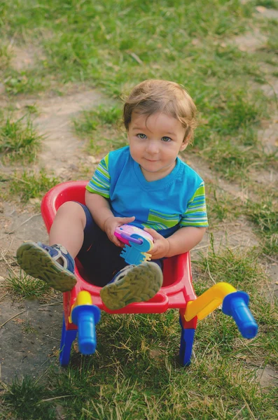 Niño pequeño jugando con carretilla de construcción de plástico para niños de colores — Foto de Stock