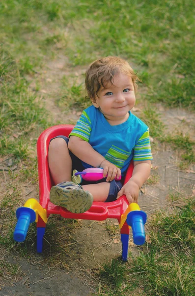 Niño pequeño jugando con carretilla de construcción de plástico para niños de colores — Foto de Stock