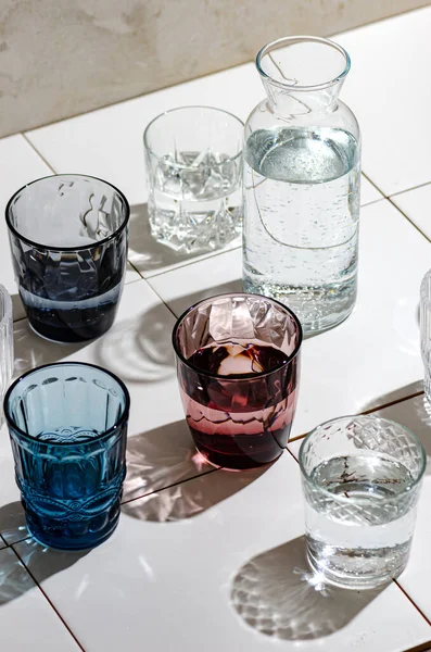 Vasos Agua Vidrio Multicolor Baldosas Blancas Rayos Duros Del Sol —  Fotos de Stock