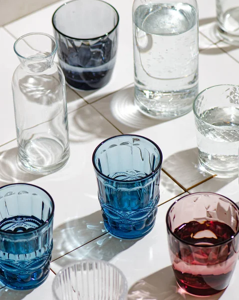 Vasos Agua Vidrio Multicolor Baldosas Blancas Rayos Duros Del Sol — Foto de Stock