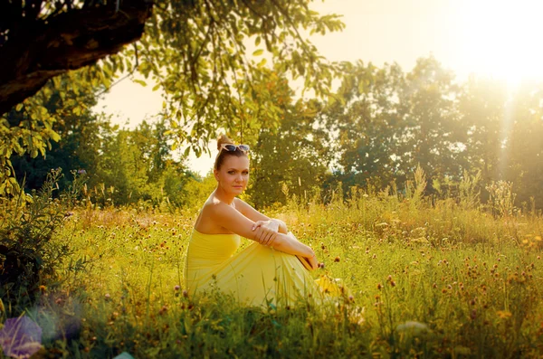 Krásná štíhlá žena ve žlutých šatech sedět na trávě v — Stock fotografie