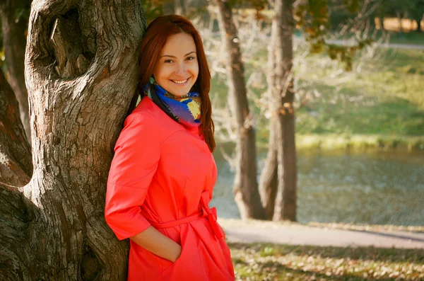 Woman in a coral coat walks on autumn park — Stock Photo, Image