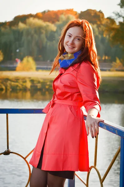 Woman in a coral coat walks on autumn park — Stock Photo, Image