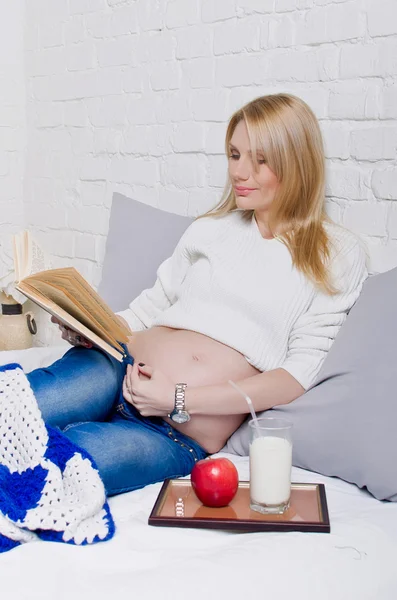 Mujer embarazada acostada en un sofá y leyendo un libro — Foto de Stock