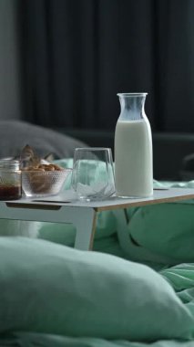 Küçük tahta bir tepside bir bardak süt, kurabiye ve bal ile yatakta sıcak bir kahvaltı. Yumuşak pastel yatak sakin bir ev atmosferi yaratır. Konfor kavramı, yavaş sabah, kişisel bakım, ev yaşam tarzı, ya da aile hafta sonu.