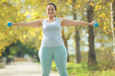 Spor tişörtlü ve taytlı çekici bir kadın spor için şehir parkında spor yapıyor..