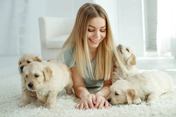 Cute young woman kisses and hugs a Labrador Retriever puppy dog. Love between owner and dog. In the room at home, interior.