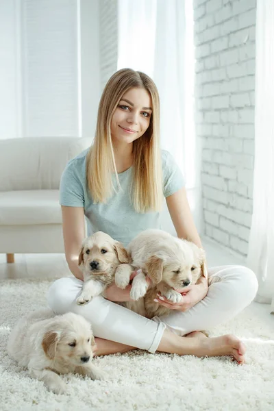 Cute young woman kisses and hugs a Labrador Retriever puppy dog. Love between owner and dog. In the room at home, interior. — Stock Photo, Image