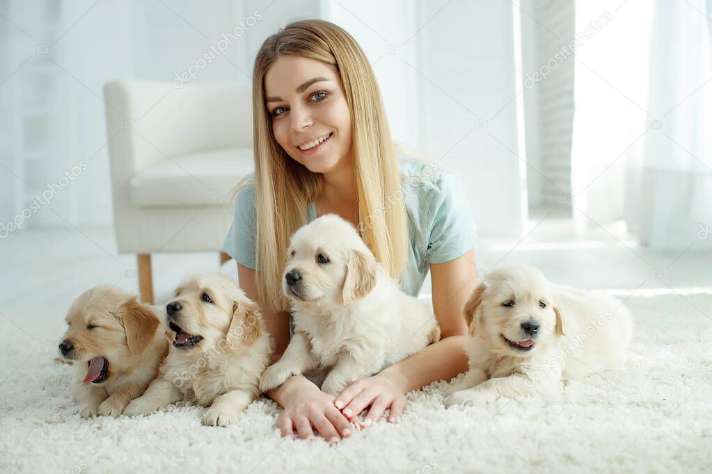 Cute young woman kisses and hugs a Labrador Retriever puppy dog. Love between owner and dog. In the room at home, interior.