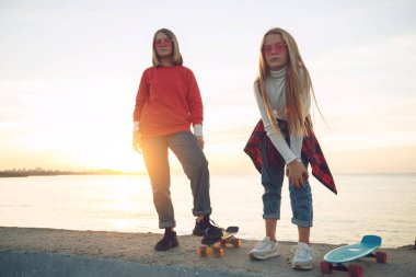 Parkta kaykayla oynayan iki bayan arkadaş. Kaykaylı kızlar. Kahkaha ve eğlence.