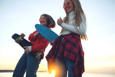 Parkta kaykayla oynayan iki bayan arkadaş. Kaykaylı kızlar. Kahkaha ve eğlence.