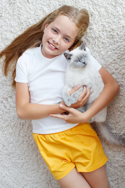Hermosa niña tendida en el suelo con un gato esponjoso. Un niño con un animal. — Foto de Stock