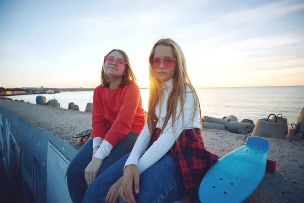 Twee vriendinnen spelen met skateboard skateboard in het park. Meisjes met een skateboard. Gelach en plezier. — Stockfoto