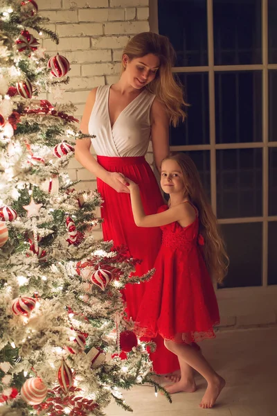 Merry Christmas and Happy Holidays. Mom and daughter with a Christmas tree indoors at night. The evening before Christmas. Portrait of a loving family nearby. — Stock Photo, Image