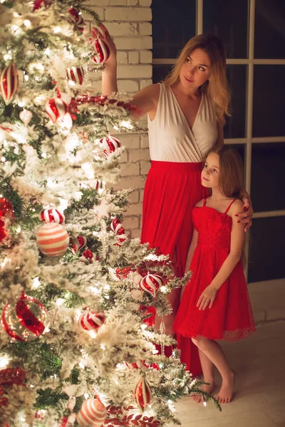 Merry Christmas and Happy Holidays. Mom and daughter with a Christmas tree indoors at night. The evening before Christmas. Portrait of a loving family nearby. — Stock Photo, Image