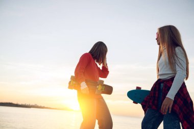 Parkta kaykayla oynayan iki bayan arkadaş. Kaykaylı kızlar. Kahkaha ve eğlence.