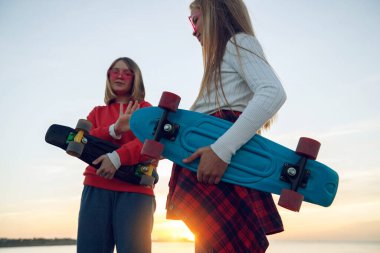 Parkta kaykayla oynayan iki bayan arkadaş. Kaykaylı kızlar. Kahkaha ve eğlence.