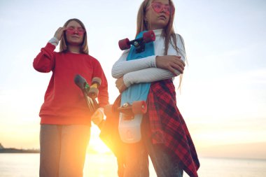 Parkta kaykayla oynayan iki bayan arkadaş. Kaykaylı kızlar. Kahkaha ve eğlence.