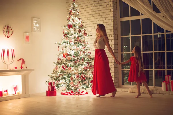 Merry Christmas and Happy Holidays. Mom and daughter with a Christmas tree indoors at night. The evening before Christmas. Portrait of a loving family nearby. — Stock Photo, Image