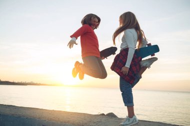 Parkta kaykayla oynayan iki bayan arkadaş. Kaykaylı kızlar. Kahkaha ve eğlence.