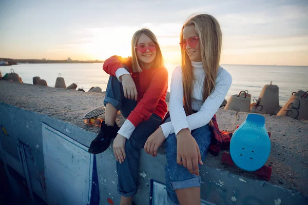 Twee vriendinnen spelen met skateboard skateboard in het park. Meisjes met een skateboard. Gelach en plezier. — Stockfoto