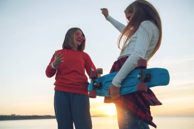 Parkta kaykayla oynayan iki bayan arkadaş. Kaykaylı kızlar. Kahkaha ve eğlence.