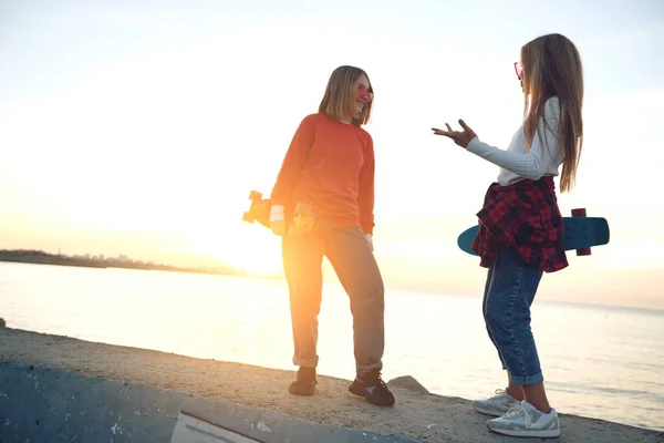 Deux amies qui jouent au skateboard dans le parc. Des filles avec un skateboard. Rire et plaisir. — Photo