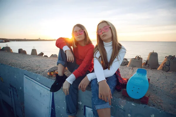 Twee vriendinnen spelen met skateboard skateboard in het park. Meisjes met een skateboard. Gelach en plezier. — Stockfoto