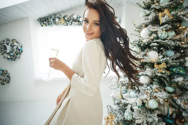 Smiling woman with glass of sparkling wine under Christmas tree lights background. — Stock Photo, Image