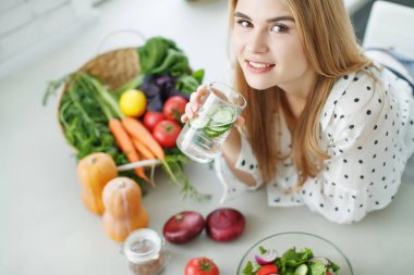  Genç bir kadın masanın yanında meyve ve sebzelerle su içiyor..