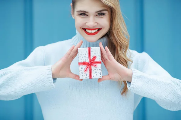 Boldog csinos fiatal nő kezében egy ajándék doboz felett kék háttér. — Stock Fotó