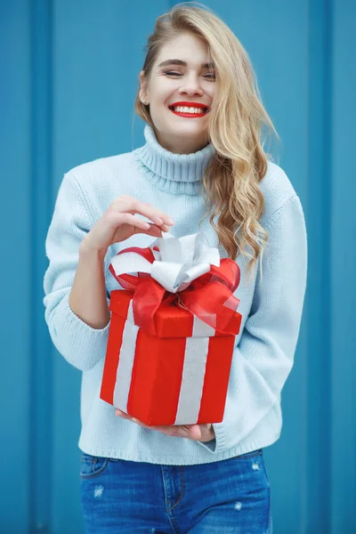 Joyeux jolie jeune femme tenant une boîte cadeau sur fond bleu. — Photo