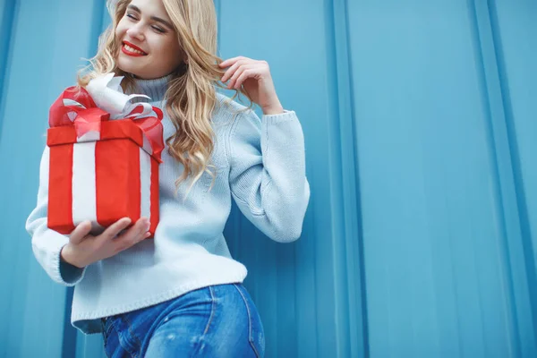 Joyeux jolie jeune femme tenant une boîte cadeau sur fond bleu. — Photo