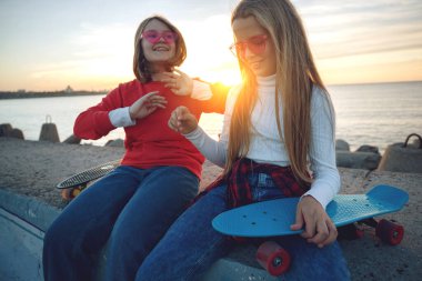 Parkta kaykayla oynayan iki bayan arkadaş. Kaykaylı kızlar. Kahkaha ve eğlence.