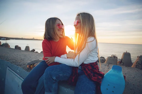 Twee vriendinnen spelen met skateboard skateboard in het park. Meisjes met een skateboard. Gelach en plezier. — Stockfoto