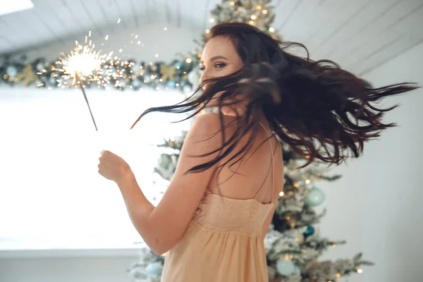 Beautiful girl brunette model posing with sparklers. Warm Christmas decor with fir tree. — Stock Photo, Image
