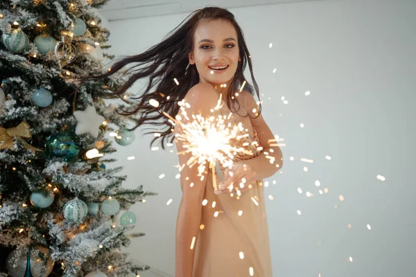 Beautiful girl brunette model posing with sparklers. Warm Christmas decor with fir tree. — Stock Photo, Image