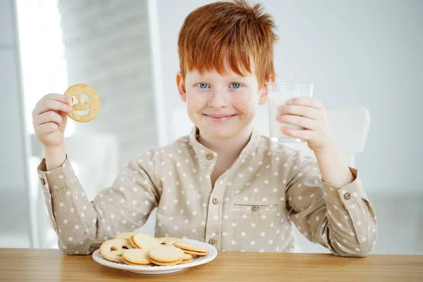 Il bambino sta facendo colazione. Il bambino beve latte e mangia biscotti. I bambini mangiano in una mattina di sole. Nutrizione sana ed equilibrata per i bambini. — Foto Stock