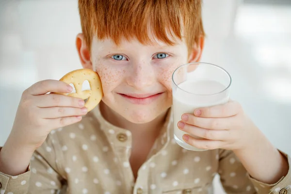 A gyerek éppen reggelizik. A kölyök tejet iszik és sütit eszik. A gyerekek napsütéses reggelen esznek. Egészséges kiegyensúlyozott táplálkozás kisgyermekek számára. — Stock Fotó
