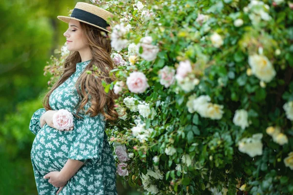 Mooie jonge zwangere vrouw in de natuur met bloemen. Zwanger meisje met rozen. — Stockfoto