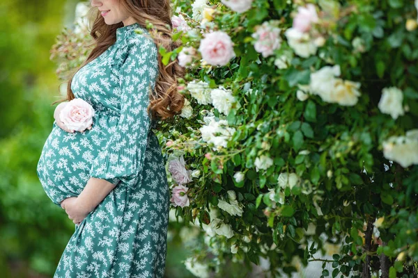 Hermosa joven embarazada en la naturaleza con flores. Chica embarazada con rosas. — Foto de Stock