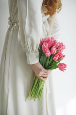 Beyaz arka planda bir buket lale tutan doğal kumaş elbiseli çekici genç bir kadın..