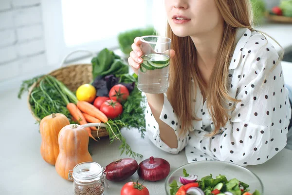 Kvinna på diet. Ung och glad kvinna äter hälsosam sallad sitter på bordet med gröna färska ingredienser inomhus — Stockfoto